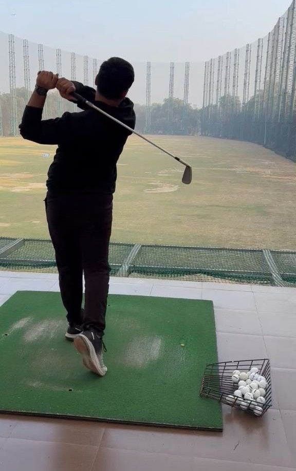 Abhinandan mid-swing at a Delhi driving range, iron held high, a basket of practice balls beside the mat
